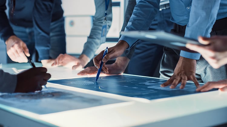 Hands trace design and engineering blueprints on backlit table