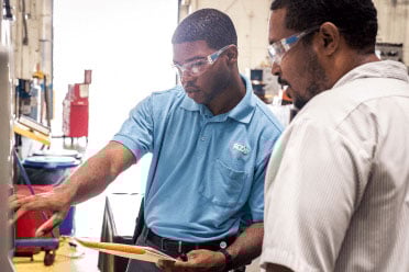 Two workers review a quality board in a plastic parts facility. Two workers review a quality board in a plastic parts facility.