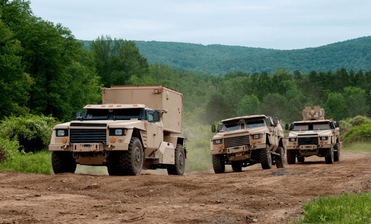 Prototype military vehicles driving through a mountain landscape.