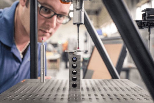 A worker checking the accuracy of a part with an automatic CMM machine. 