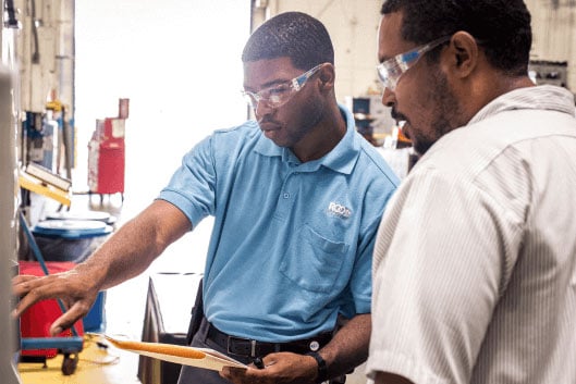 Two workers review a quality board.