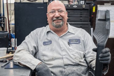 A sheet metal worker holds a part and smiles for the camera. A sheet metal worker holds a part and smiles for the camera.